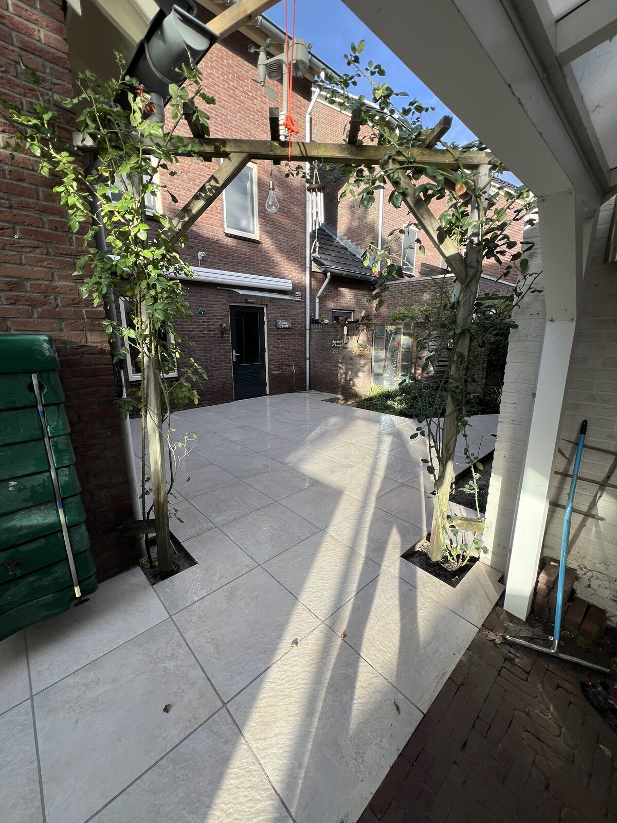 Keramische tegels onder een witte pergola langs het huis
